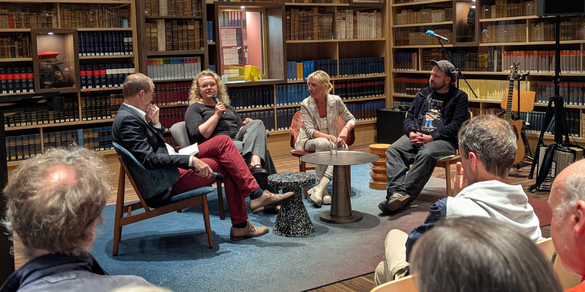 Vier Menschen sitzen in Bibliothek auf einer Bühne