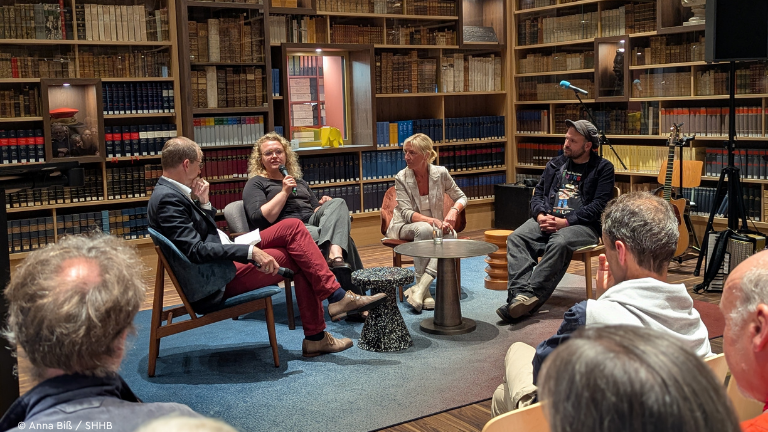 Vier Menschen sitzen in Bibliothek auf einer Bühne