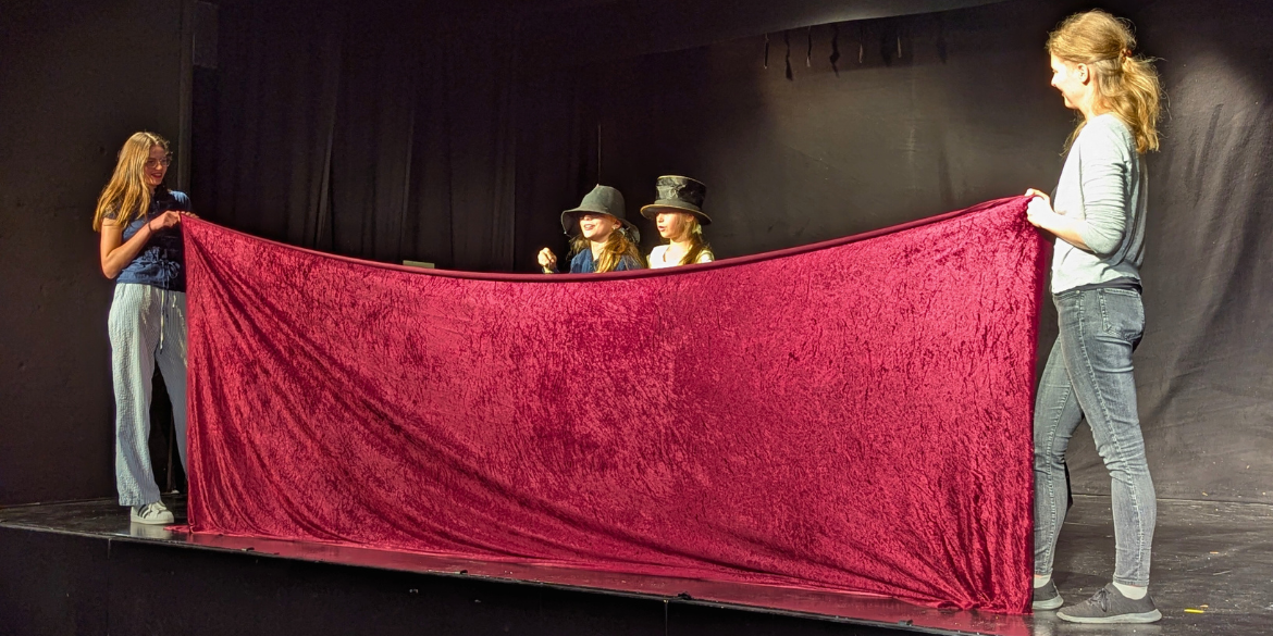 Zwei Frauen halten rotes Tuch, dahinter stehen zwei verkleidete Kinder