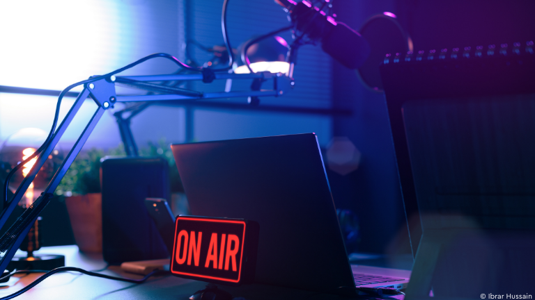 Schreibtisch mit Laptop, Mikrofon und Leuchtschild "ON AIR"